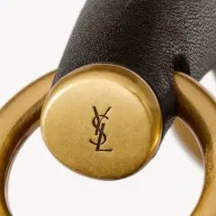 Złote logo YSL na czarnym pasku, element luksusowej torebki. YSL to francuski dom mody.