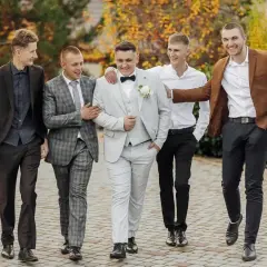 Pięciu mężczyzn w eleganckich strojach na wesele jako goście. Jeden w jasnej, dwurzędowej marynarce, inny w brązowej.