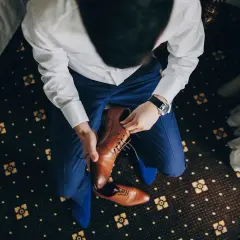 Mężczyzna w niebieskim garniturze i białej koszuli zakłada brązowe, eleganckie buty. Idealne pytanie: jakie buty do niebieskiego garnituru?