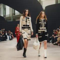 Dwie modelki prezentują kreacje francuskiego domu mody na wybiegu. Eleganckie sukienki w stylu Chanel, bogata biżuteria i torebki.