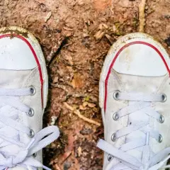 Białe trampki z czerwonymi akcentami, lekko zabrudzone ziemią, czekają na czyszczenie.