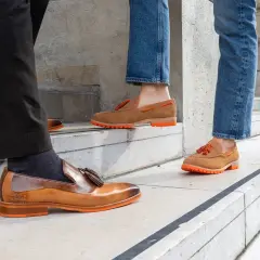 Eleganckie mokasyny z frędzlami i ozdobnym elementem horsebit, w brązowych i rudych odcieniach, na pomarańczowej podeszwie.