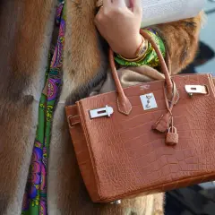 Elegancka torebka marki Hermes w kolorze koniaku, wykonana ze skóry krokodyla, z charakterystycznym zapięciem i małą kłódką.