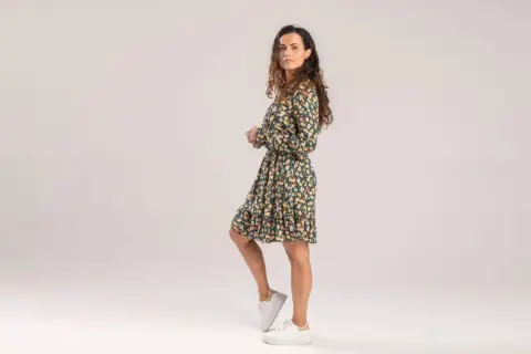 Kobieta w kwiecistej sukience i białych sneakersach. Czy sukienki w kwiaty są modne? Tak, ta stylizacja to dowód!