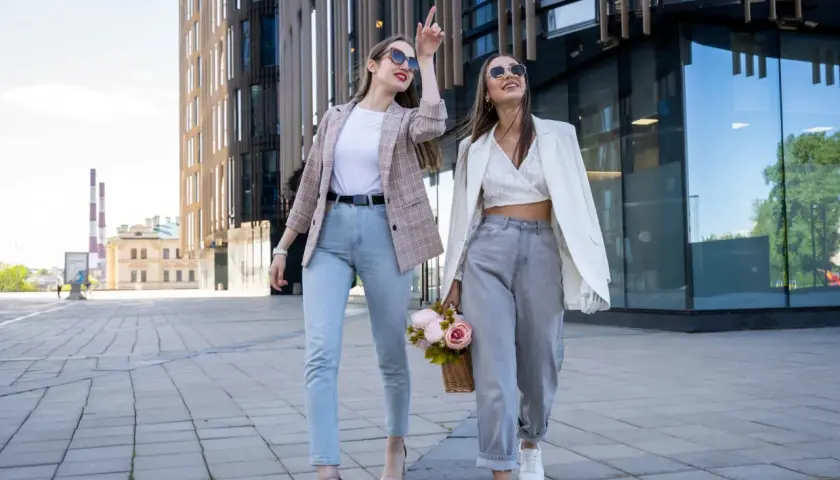 Dwie kobiety w modnych stylizacjach spacerują przed nowoczesnym budynkiem. Ich ubiór sugeruje, że to polskie marki znane na świecie.