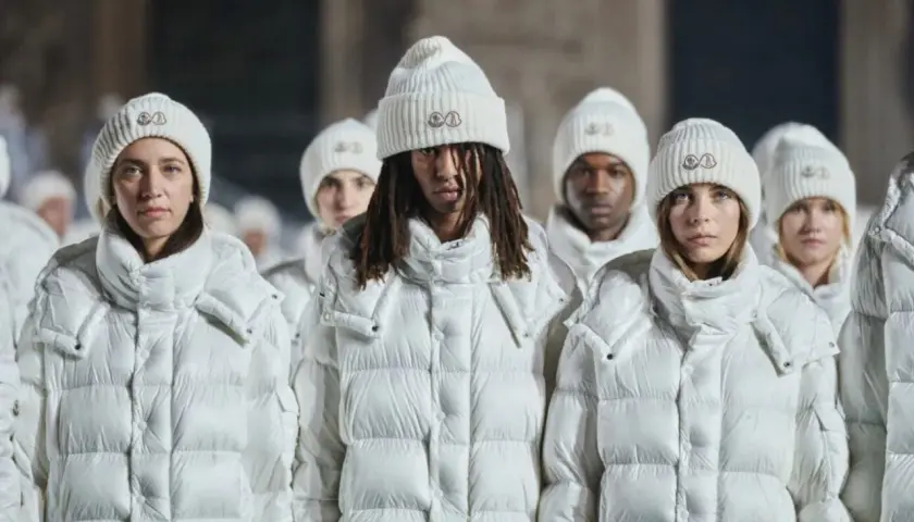 Grupa osób w białych kurtkach i czapkach Moncler. To właśnie moncler co to za firma – marka znana z luksusowej odzieży zimowej.