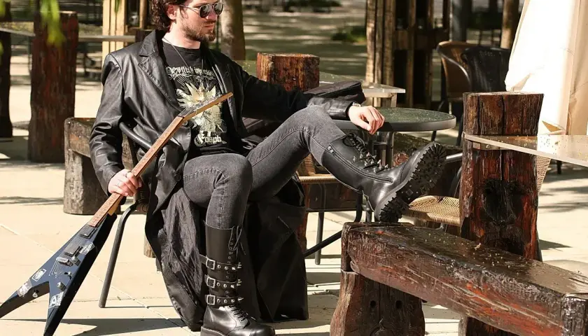 Mężczyzna w skórzanej kurtce i czarnych jeansach, idealnych jako spodnie do glanów, siedzi z gitarą.