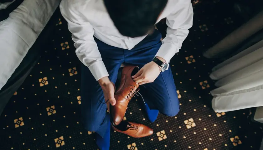 Mężczyzna w niebieskim garniturze i białej koszuli zakłada brązowe, eleganckie buty. Idealne pytanie: jakie buty do niebieskiego garnituru?