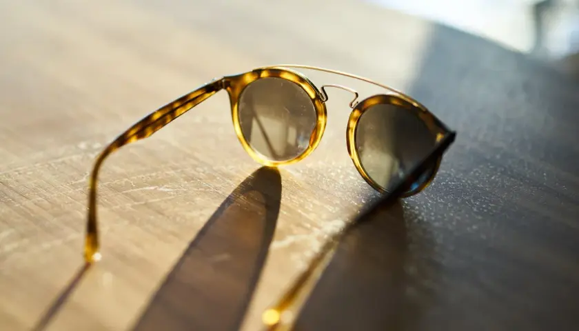 Okulary przeciwsłoneczne w stylu retro, z oprawkami w panterkę i złotymi elementami, leżą na drewnianym blacie. To jedne z tych znanych marek okularów przeciwsłonecznych, które dodają stylu.