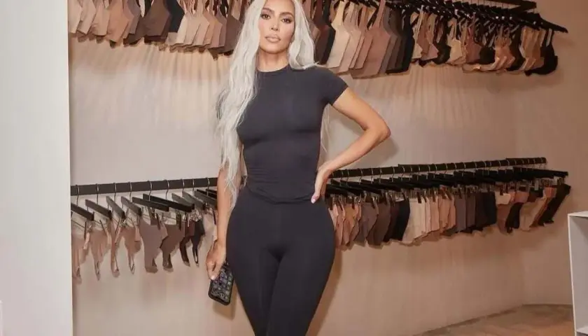 Kim Kardashian w czarnym dopasowanym stroju, na tle wieszaków z bielizną. Skims w Polsce gdzie kupić? Sprawdź ofertę!