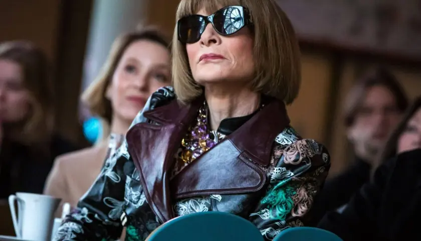 Anna Wintour w okularach przeciwsłonecznych i wzorzystej kurtce, ikona Vogue, wpatruje się w dal.
