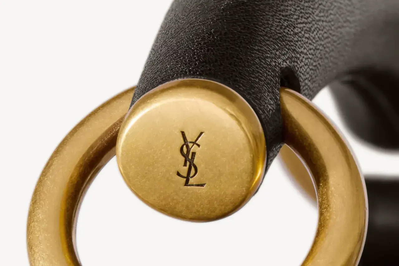 Złote logo YSL na czarnym pasku, element luksusowej torebki. YSL to francuski dom mody.
