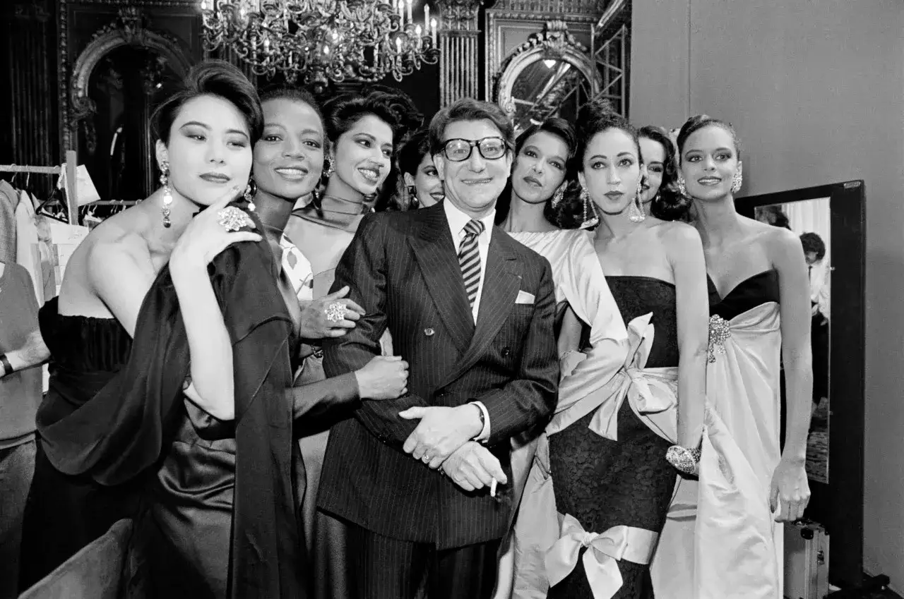 Yves Saint Laurent, znany z elegancji, otoczony modelkami w kreacjach YSL. To kwintesencja tego, ysl co to za firma.