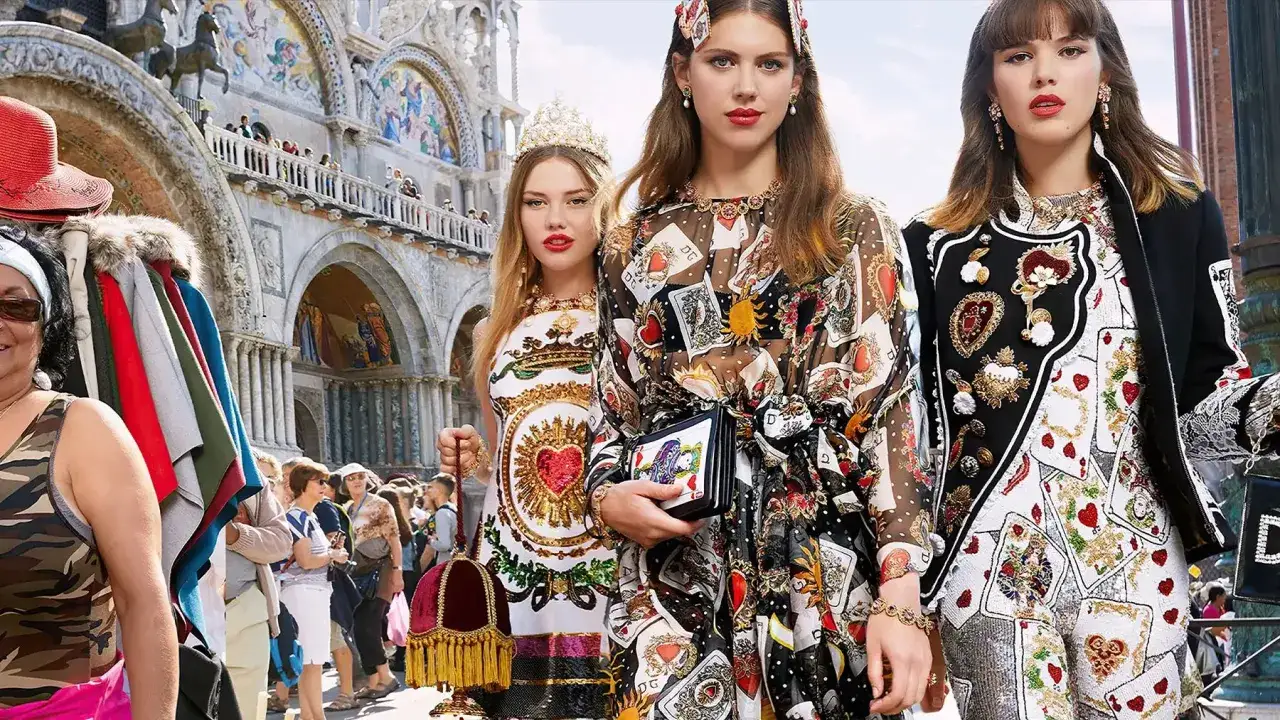 Trzy kobiety w strojach z motywem kart do gry, w stylu Dolce & Gabbana, pozują na tle weneckiej bazyliki.